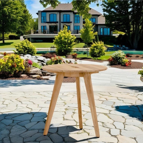 14916 surf teak side table on stone patio surrounded by landscaping plants with pool and house in background