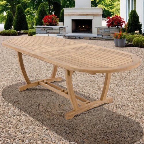 15504 Montserrat Extension Table angled on stone patio with fireplace and landscaping plants and trees with house in background