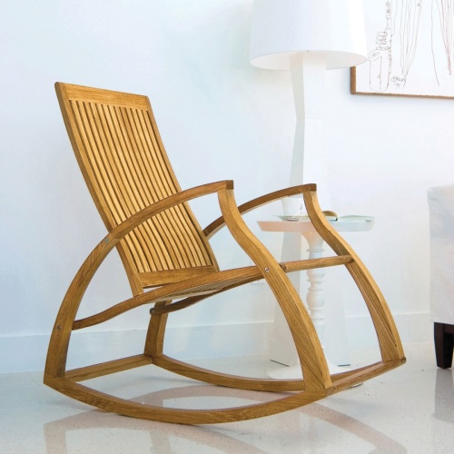 16419 Aria Teak Rocker against white wall with artwork sitting on marble floor next to white side table and lamp in an inside room