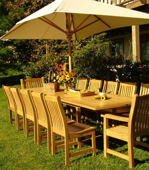 17640 grand rectangular teak umbrella six point five feet by ten feet in rectangular dining set with basket of wine flowers in vase and candle on grass with trees in background 