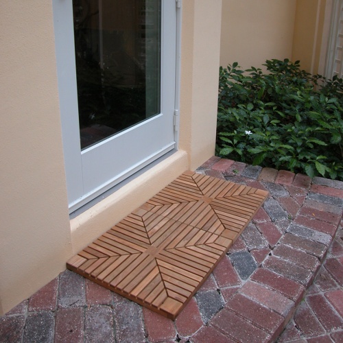 18408DM Teak Diamond Door Mats showing 2 outside of entry door on brick step with house and landscape plants in background