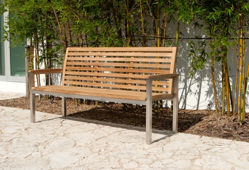 23200RF Vogue teak and stainless steel 5 foot bench refurbished angled on stone pavers with bamboo trees against wall in background