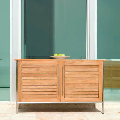 28225RF Vogue teak and stainless steel Sideboard on outdoor patio with white bowl of apples on top against glass windows