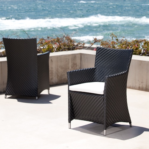 29001BKDP Valencia Black Armchair with seat cushion showing two on a concrete terrace surrounded by landscape plants with ocean and blue sky background