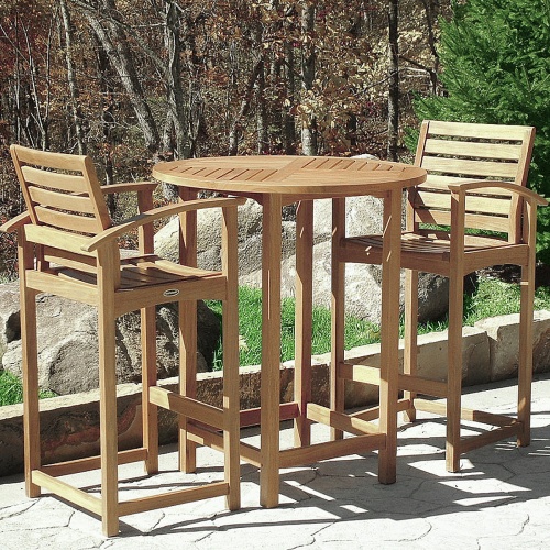 70011 Somerset 3 piece teak Bar Set on stone walkway in front of 3 large rocks on grass and bare trees and natural vegetation in background 