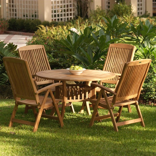 70025 Hyatt Recliner teak 5 piece round Dining Set on grass yard showing a white plate of green apples on table with trees and shrubs in background
