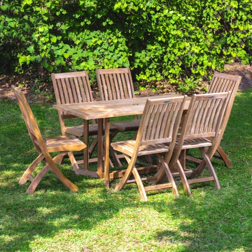 70039 Nevis Barbuda 7 piece Dining Set of 6 teak folding side chairs and a folding 5 foot long rectangular dining table on grass lawn with shrubs and trees in background