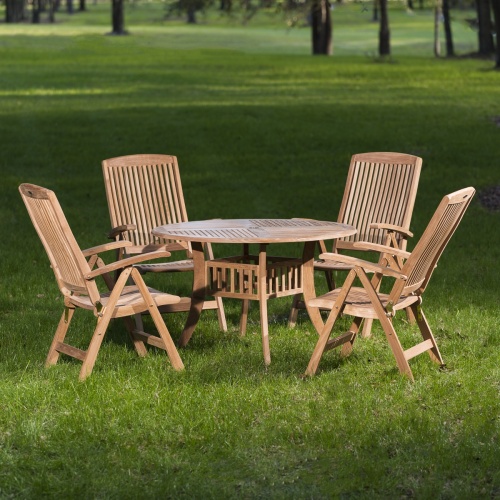 70045 Hyatt Recliner 5 piece teak Dining Set of 4 teak reclining armchairs and a round 48 inch diameter dining table on grass field with trees in background 