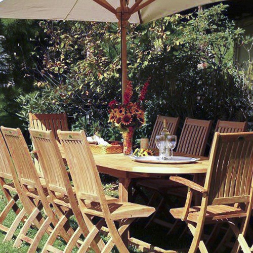 70050 Montserrat Barbuda 11 piece teak dining set with market umbrella vase of fresh flowers pillar candle silver tray with wine bottle and glasses outside shrubs in background  