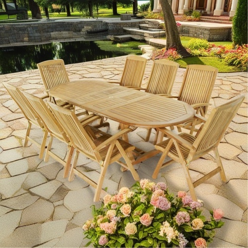 70163 Montserrat 9 pc teak Dining Set of Montserrat oval dining table and 8 Reclining Side Chairs side angled on paver patio and pond and shrubs in background 