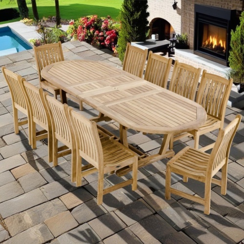 70166 Montserrat 11 piece teak oval Dining Set of Montserrat Oval Dining Table and 10 Veranda side chairs on patio with pool and fireplace with landscape plants and grass lawn in background