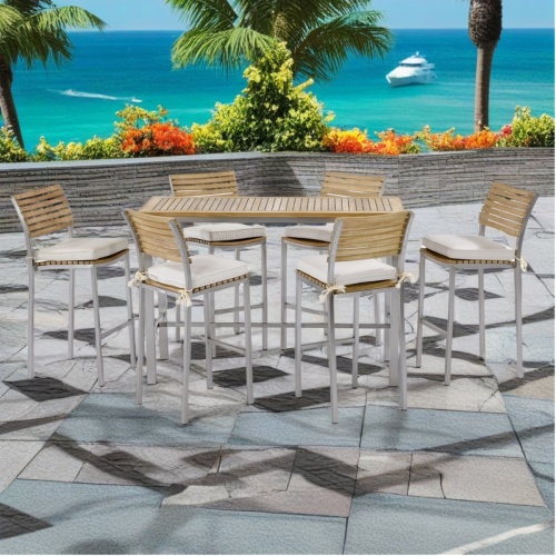 70167 Vogue 7 piece stainless steel and teak Bar Table Set of Vogue Dining Table side view with optional canvas color cushions on patio with palm trees landscape shrubs and ocean in background