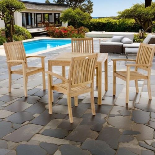 70210 Sussex teak 5 piece square Dining Set of 4 teak armchairs and a teak 36 Inch square dining table on patio with pool surrounded by plants with furniture and house in background
