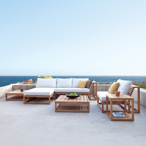 70231 Maya Deep Seating 6 piece teak Lounge Set with cushions with 2 potted succulents on 2 side tables and a coffee table with a black bowl of green apples on terrace with plants and ocean and blue skies in background