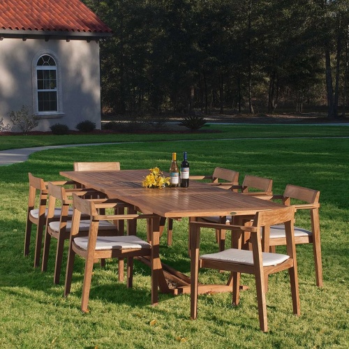 70237 Grand Horizon teak 9 piece Dining Set with optional canvas colored cushions yellow flowers two wine bottles on grass lawn house and landscaped background