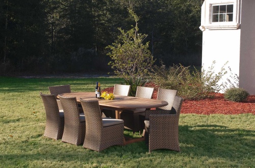 70244 Montserrat Valencia 9 Piece Dining Set on grass lawn showing 2 wine bottles and yellow flowers on top with landscape plants and trees and part of a white house in back