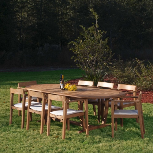 70255 Montserrat Horizon 9 piece Teak Dining Set with optional seat cushions on grass field with trees and shrubs in background
