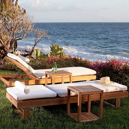 70308 Horizon teak double chaise set cushioned with hat and two side tables with bottle water and glass angled on lawn with flowering plants trees ocean and blue sky in background