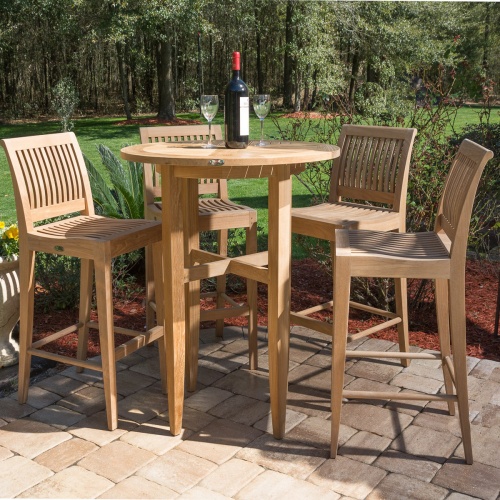 70416 Laguna 5 piece teak High Bar set with wine bottle and two glasses on paver patio surrounded by landscape plants and grass and trees in background