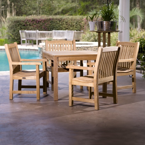 70425 Veranda 5 piece Square Dining Set on concrete patio and tall table with 5 potted plants next to table with pool and bushes trees and landscape plants in background