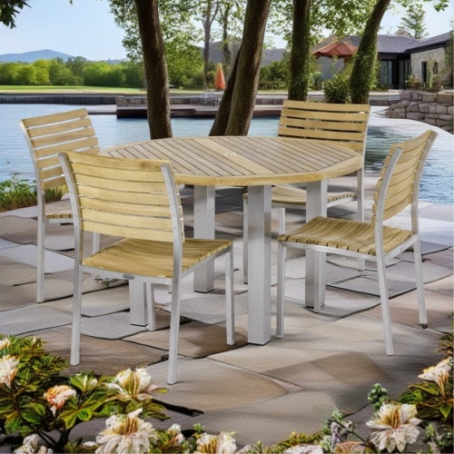 70438 Vogue teak and stainless steel 5 piece Dining Set of 4 side chairs with optional seat cushions and round 48 inch diameter table on patio surrounded by flowers with house and water in background