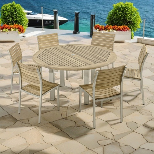 70439 Vogue stainless steel and teak 7 piece round Dining Set of 6 dining side chairs and round 60 inch diameter dining table angled view on stone patio with boat and dock in background