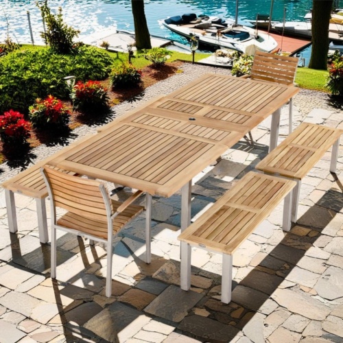 70440 Vogue 7 piece Teak and Stainless Steel Picnic Set on stone patio surrounded by plants and trees overlooking the ocean with boats at a dock in background  