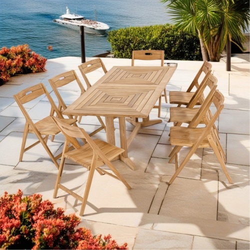 70464 Surf Pyramid Teak Dining Set for 8 angled end view on patio terrace surrounded by plants and trees overlooking ocean with yacht in background  