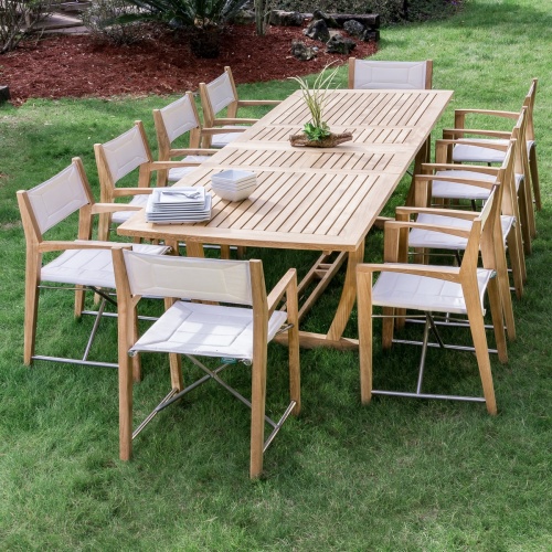 70466 Odyssey 11 piece teak dining set with green plants in wood branches centerpiece white square plates bowls on grass lawn and landscaped mulch area in background
