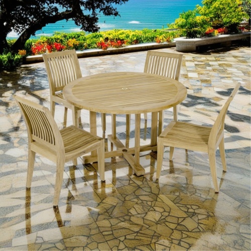 70482 Laguna 4 foot round teak Dining Set of a 4 foot round teak dining table and 4 teak side chairs side view on stone patio with ocean and trees in  background