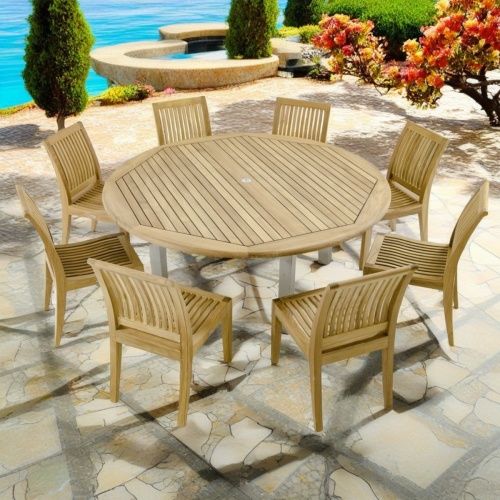 70488 Vogue Laguna Dining Set of 8 teak side chairs and a teak 72 inch round dining table angled side view on stone patio with trees and shrubs in  background 