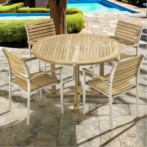 70491 Vogue Dining Set of a teak and stainless steel Round Dining Table and 4 Vogue teak and stainless steel chairs on stone pool deck with pool and plants in background