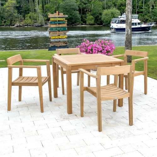 70495 Horizon 5 piece Square Cafe Set of 4 teak armchairs and 36 inch square dining table on paver patio with flowering potted plant overlooking lake with boat and trees in background