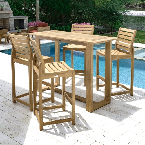  70512 Somerset 5 piece teak Barstool and Bar Set angled view next to pool with fireplace teak chairs and flowering plants and shrubs in background 