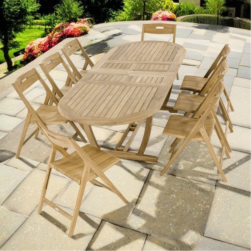 70516 Montserrat Surf 9 pc Dining Set of Montserrat teak ova table and 8 Surf folding chair angled end view on stone patio with plants in  background   