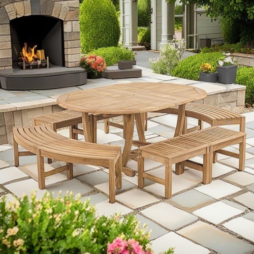 70522 Martinique 7 pc Bench Dining Set of Martinique Oval Dining Table and 4 Backless Benches and 2 Backless Curved Benches on paver patio with plants and trees and a fireplace in back