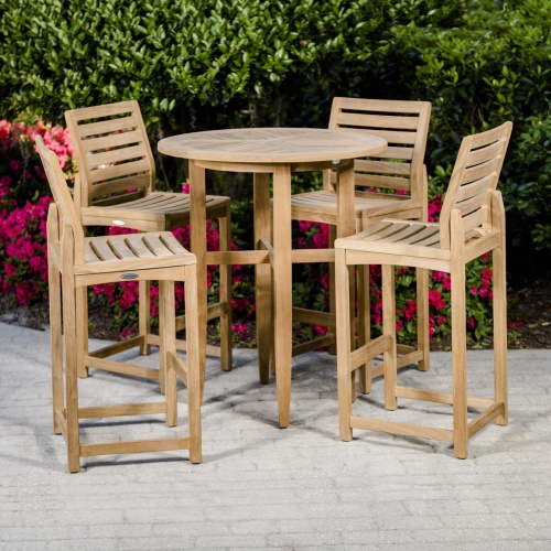 70532 Teak 5 piece Bar Table Set of 4 Somerset barstools and Laguna Table on patio with flowering plants and landscape shrubs in background