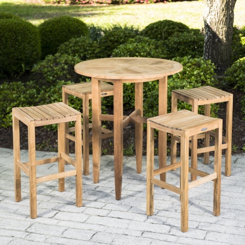 70533 Somerset Laguna 5 piece teak Bar Set of 4 teak backless barstools and round 36 inch diameter bar table on white brick patio with shrubs in background