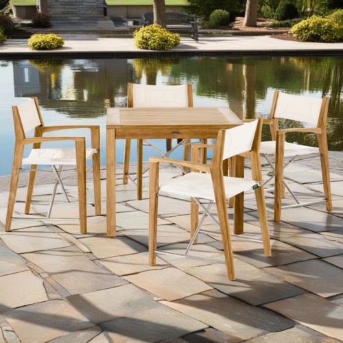 70540 Odyssey teak Dining Set of a Teak 36 Inch square dining table and 4 chairs angled view on patio with landscape plants and water in the background
