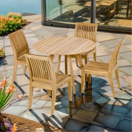 70541 Laguna Surf  Dining Set of a Surf teak 42 inch round dining table and 4 Laguna Dining Chairs angled on paver patio surrounded by flowering plants with glass door in  background