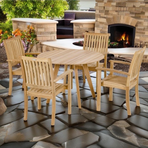70547 Sussex Surf 5 pc Dining Set of a round Surf teak 42 inch diameter dining table and 4 Sussex Chairs side view on stone patio with fireplace and sitting area in background