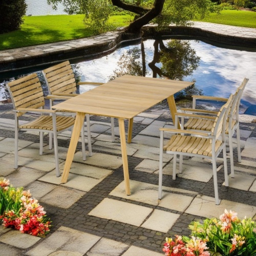  70563 Surf Vogue Dining Set of Surf teak 5 foot rectangular dining table and 4 Vogue Side Chairs angled side view on square pavers next to pool with trees and shrubs in background 