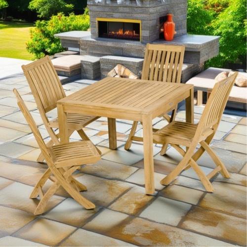 70570 Barbuda 5 piece Dining Set of a Barbuda teak 36 inch square dining table and 4 Side Chairs angled view on patio with outdoor fireplace grass and trees in the background