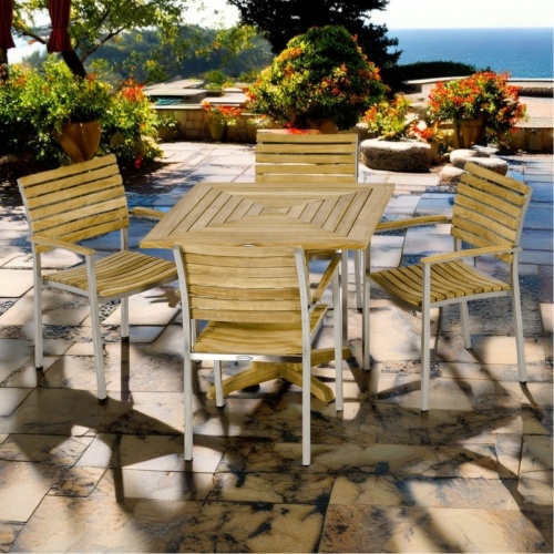  70575 Vogue Pyramid Dining Set of Pyramid teak 36 inch square dining table and 4 Vogue Chairs angled on patio terrace surrounded by trees overlooking ocean in background  