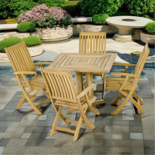 70576 Barbuda Pyramid teak Dining Set of a 36 inch square dining table and 4 Barbuda Chairs angled view on stone patio planters with shrubs and landscape plants in background
