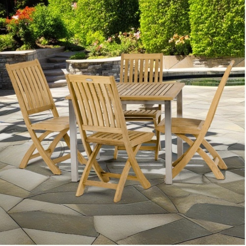 70579 Vogue Barbuda Dining Set of a teak and stainless steel 36 inch square dining table and 4 Barbuda folding chairs on stone patio with landscape plants in background