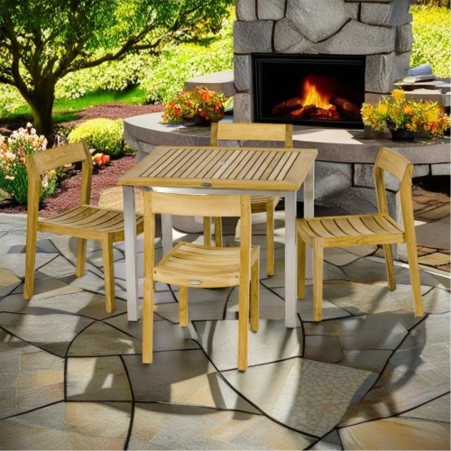 70588 Vogue Horizon Dining Set of a teak and stainless steel 36 inch square dining table and 4 teak Horizon Side Chairs angled view on pavers with outdoor fireplace in background