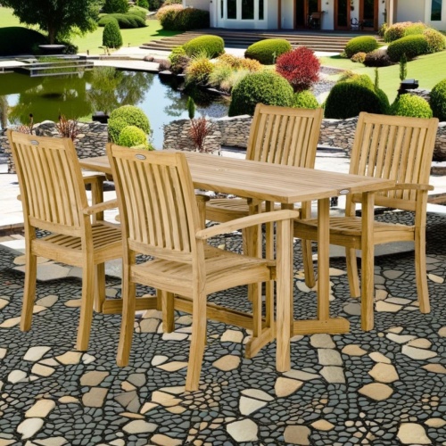  70607 Sussex Nevis 5 pc Dining Set of a Nevis teak folding 60 inch rectangular dining table and 4 Sussex dining armchairs angled on stone patio surrounded by plants in background  