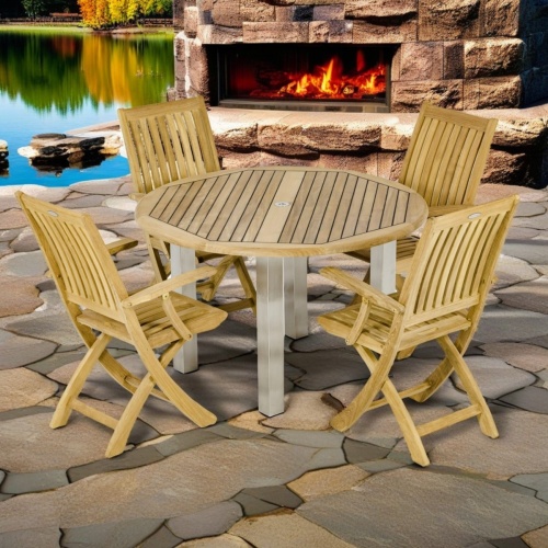 70623 Vogue Barbuda 5 piece Dining Set side view of 4 teak folding armchairs and a teak and stainless steel 48 inch round dining table on stone patio with fireplace and lake in background 