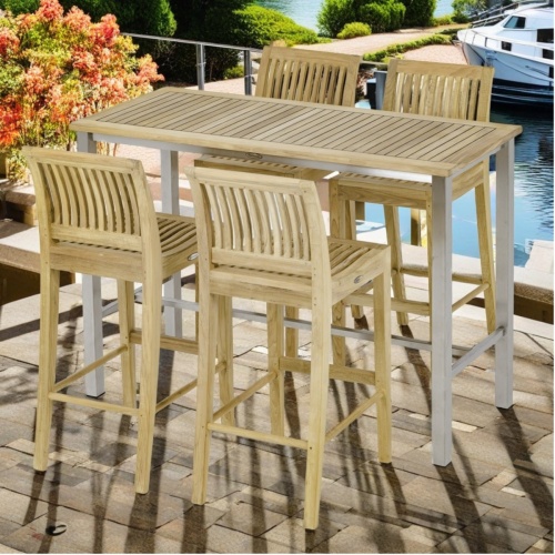 70633 Vogue Laguna 5 piece Bar Set of 4 teak side barstools and a teak and stainless steel 5 foot long rectangle table angled side view on boat dock with boats and water in background